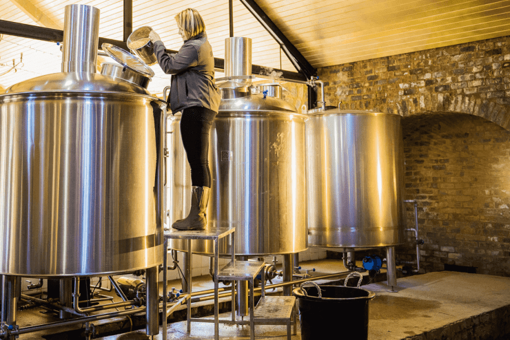 A woman pouring an ingredient into a distilling vessel - distilleries