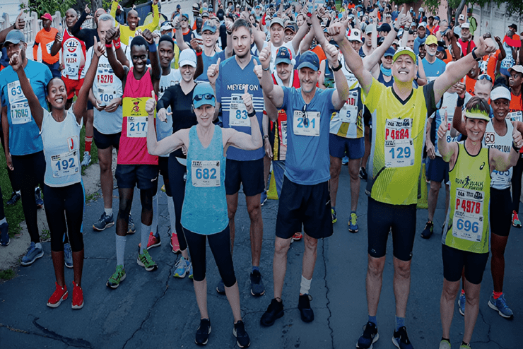 A large group of athletes standing at the marathon starting line, posing for the camera with their arms raised