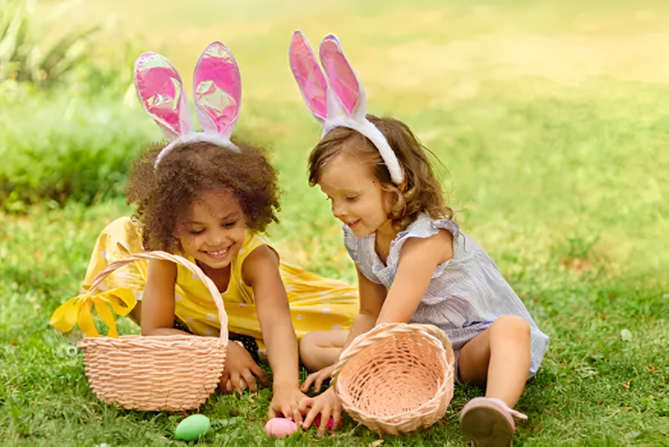 Two young girls wearing bunny ears collecting Easter eggs and placing them in their baskets