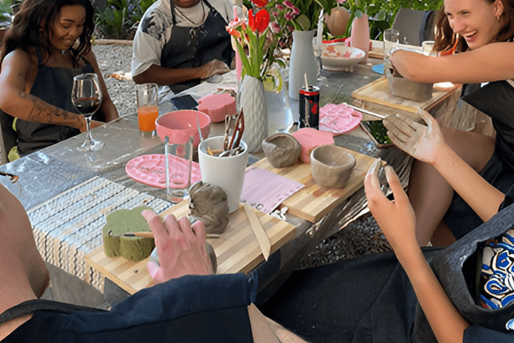 A group of people sit at an outdoor table, making ceramics