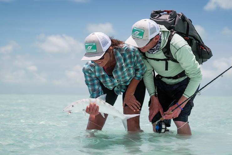 Two people hold and observe a fish whilst stood in a body of water - July events