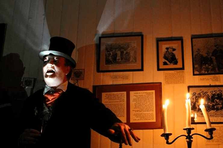 The mystery ghost tour host flashes a torch in his face as he stands in front of some tour props